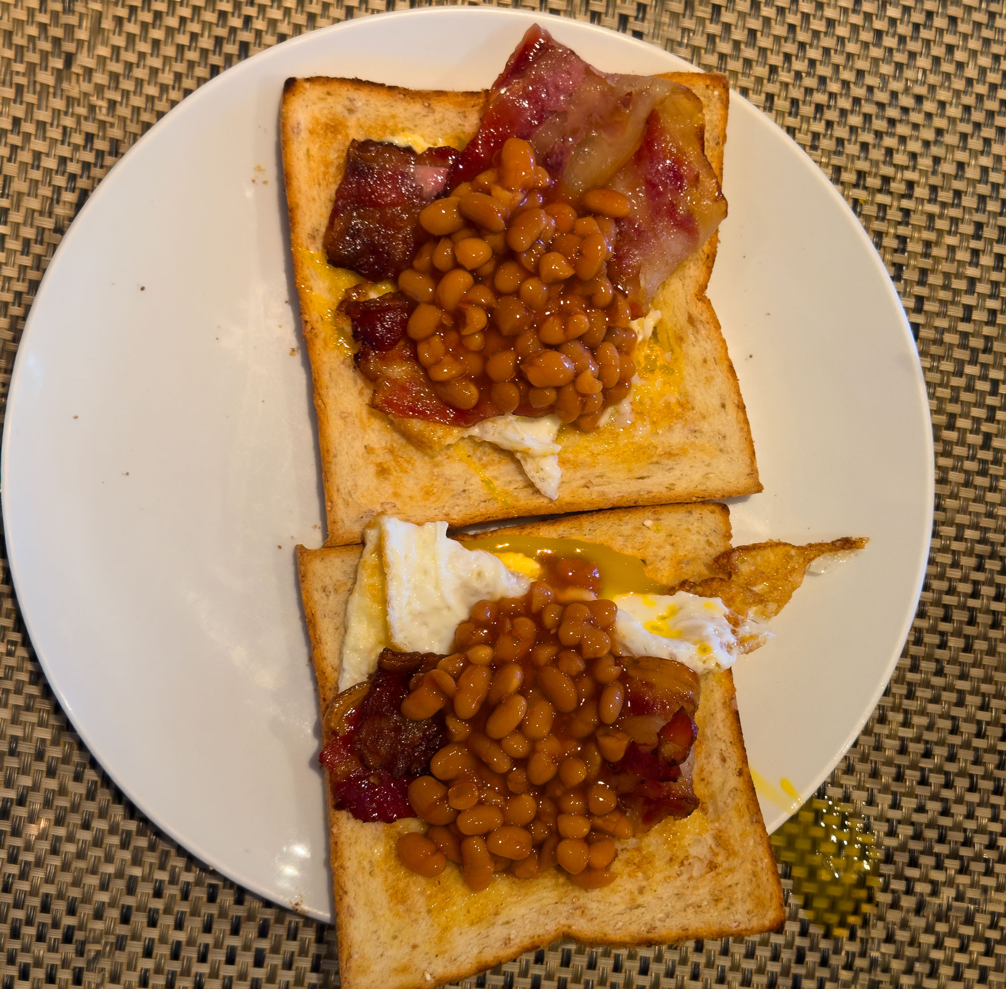 the runny eggs and baked beans topped with crispy bacon on toast breakfast sandwich